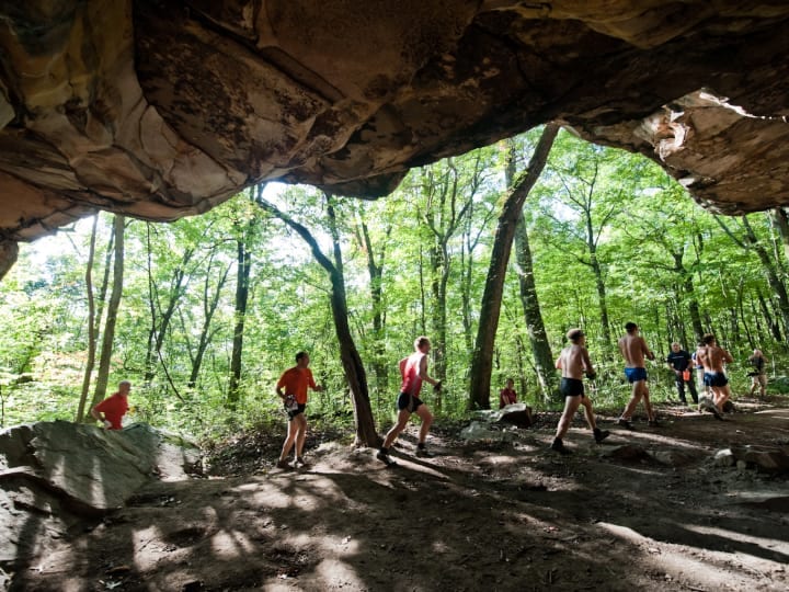 People running past the large opening of a cave. Photographer is in the cave looking out.